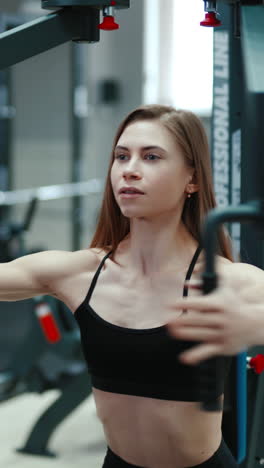 a pretty woman with flowing hair is sitting and doing exercise for the chest in the gym. professional equipment. healthy lifestyle vertical video