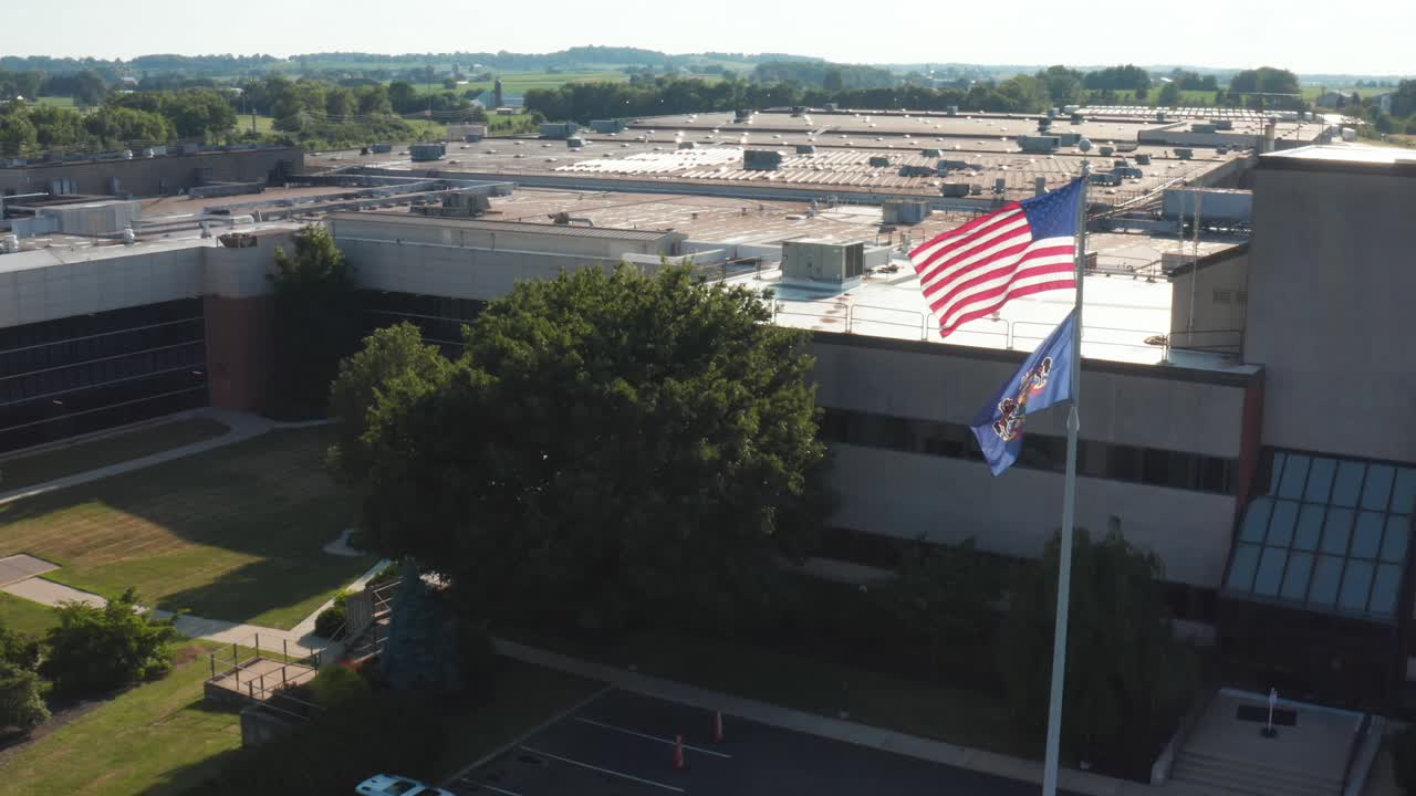 USA and Pennsylvania flags fly in breeze at large industrial production facility workplace