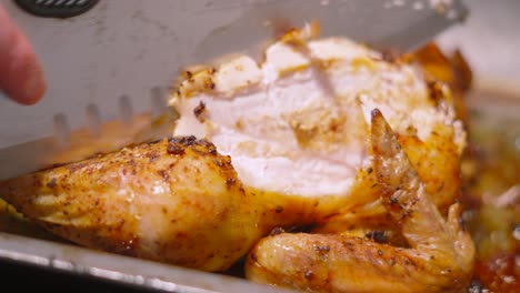 carving knife cutting chicken meat from whole roasted chicken in roasting pan with legs and wings