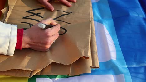 female caucasian hand writes anti-war protest placard, close up shot