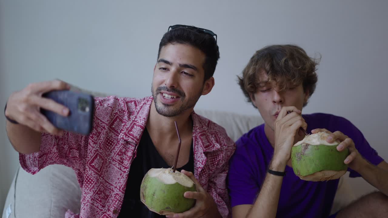 Two men taking a selfie and enjoying coconut drinks indoors