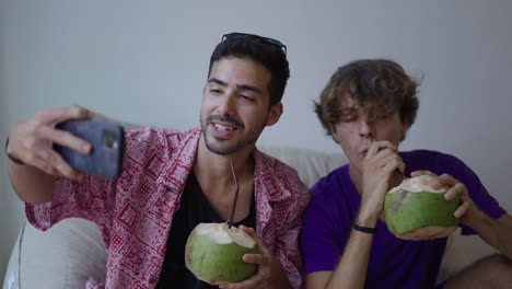 two men taking a selfie and enjoying coconut drinks indoors