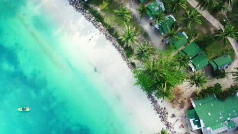 Beach-bungalows-on-shore-of-tropical-island-with-white-sand-washed-by-calm-turquoise-lagoon-and-palm-trees-in-Malaysia