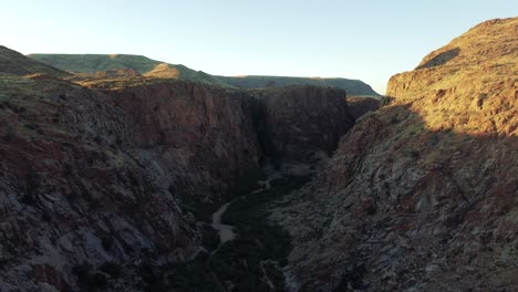 cinematic aerial view flying over a lush desert gorge between two cliffs at golden hour at riemvasmaak park in south africa near namibia