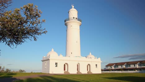 reveal shot showing white lighthouse on green hill with blue sky