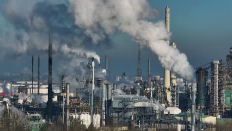 Medium-aerial-shot-of-steam-and-smoke-from-a-dense-industrial-facility-with-many-stacks-and-towers-on-a-sunny-but-hazy-day-outside-of-Rotterdam-Netherlands