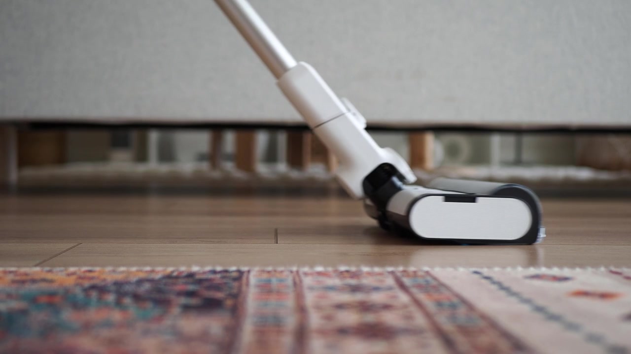 Cordless Stick Vacuum Cleaning Under Furniture on Wooden Floor