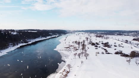 flowing winter river and landscape during snowfall, aerial drone view