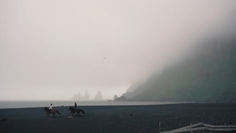 Horses-running-in-SlowMotion-across-black-sand-beach,-in-a-foggy-day-in-Vik,-Iceland