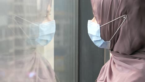 woman in hijab and face mask looks out window