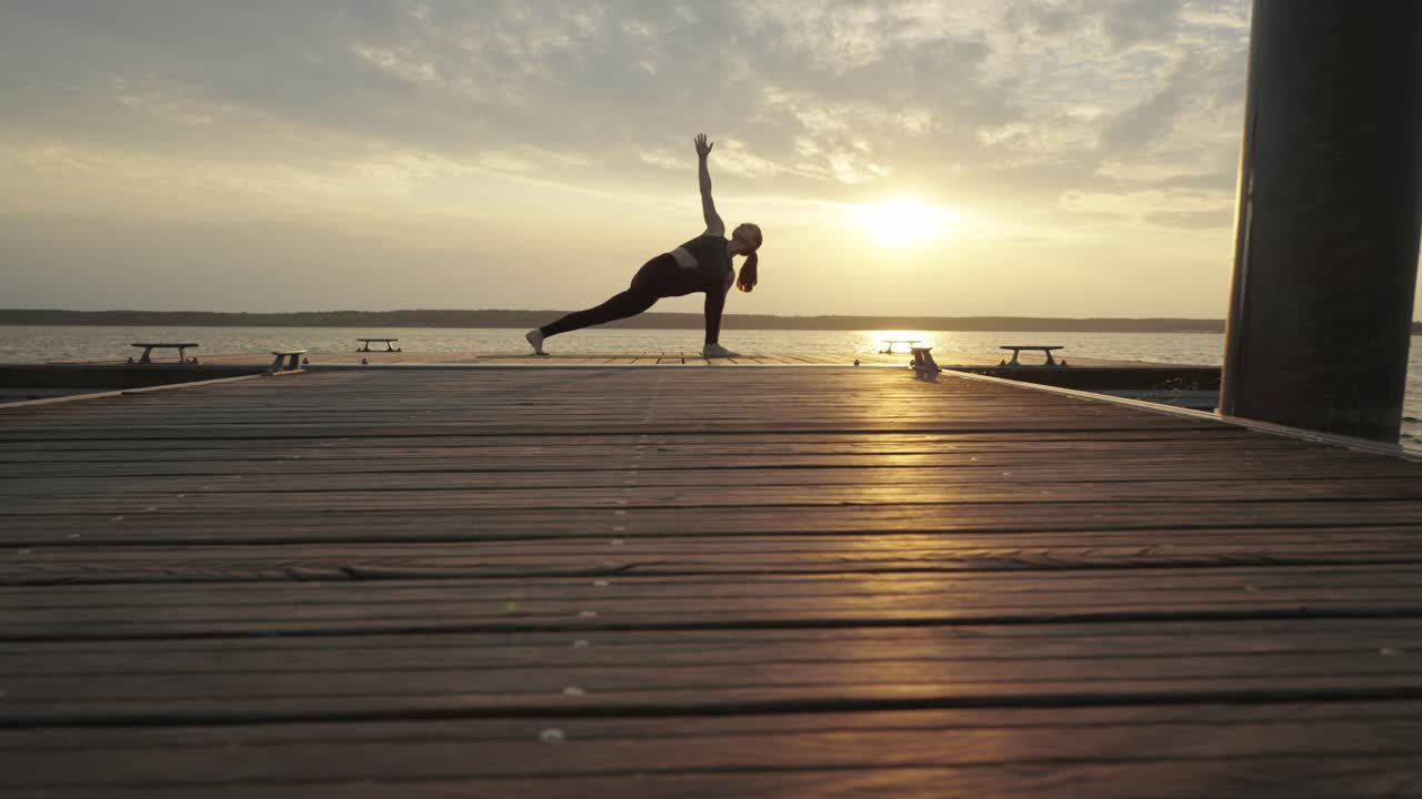 mujer joven haciendo estiramientos de yoga en el muelle al atardecer, con vistas al mar en calma