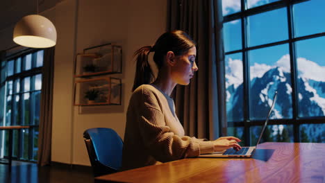 woman working on laptop by a window with a majestic mountain view
