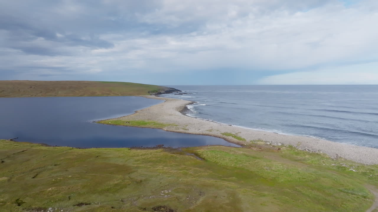 Still drone aerial view of the Barvas estuary on the Isle of Lewis, Outer Hebrides. Loch Mor Bharabhais meets the Atlantic Ocean through a gravel spit under soft Hebridean light and calm blue skies