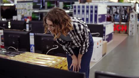 Cliente-Femenino-Moderno-E-Inteligente-Que-Elige-Televisores-Grandes-En-Una-Tienda-De-Electrónica.-Nuevas-Generaciones-De-Pantallas.-Mire-De-Cerca-Un-Televisor-Grande-Y-Delgado