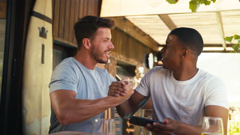 Two-Male-Friends-Outdoors-At-Home-Watching-Sports-On-Mobile-Phone-Celebrating-Team-Win