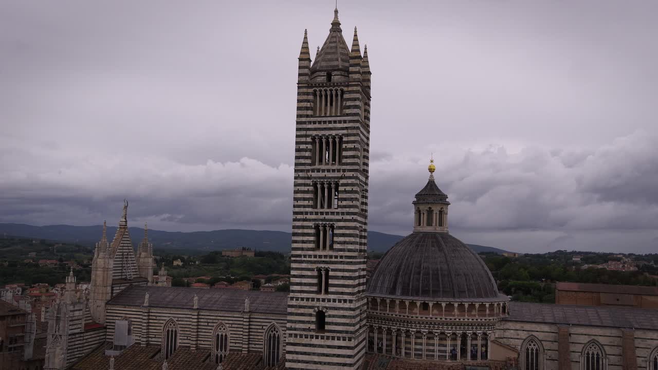 Siena cathedral's striped bell tower against a cloudy sky in scenic tuscany, aerial view