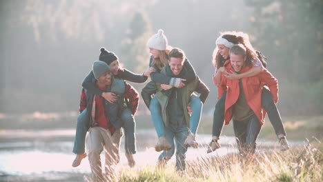 Sechs-Freunde-Haben-Spaß-Beim-Huckepackfahren-Auf-Dem-Land-Am-See