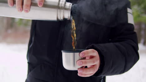 man pouring hot drink from thermos into cup in winter