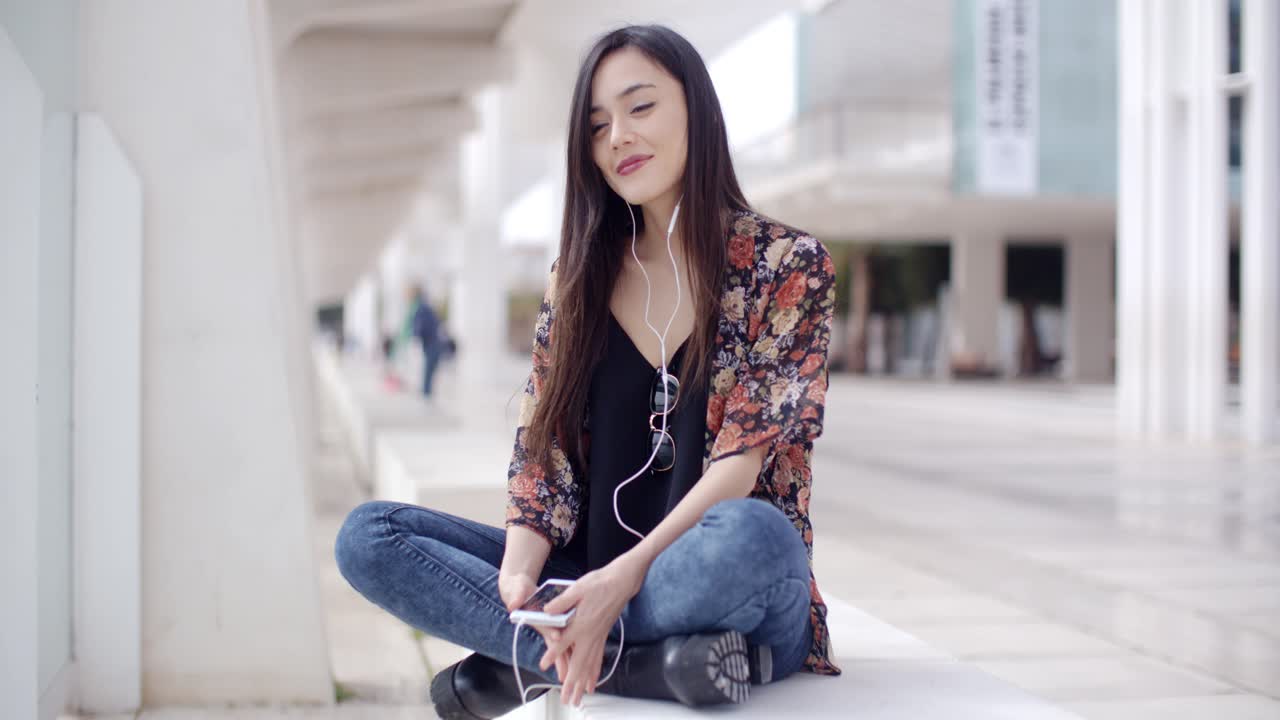 트렌디한 젊은 여성이 마을에서 음악을 듣고 있습니다.