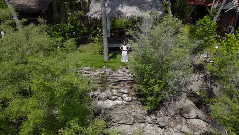 a woman in white, standing under a thatched pavilion on cebu island, philippines, surrounded by lush greenery, aerial view