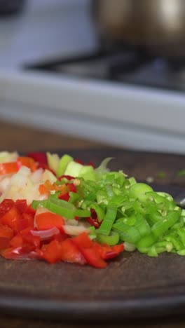 fresh vegetables are being chopped and prepared on a wooden cutting board in a cozy kitchen setting. the blurred pot in the background adds a warm and inviting atmosphere to the cooking process