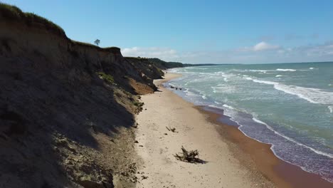 Flying-Over-Coastline-Baltic-Sea-Ulmale-Seashore-Bluffs-Near-Pavilosta-Latvia-and-Landslides-With-an-Overgrown,-Rippling-Cave-Dotted-Cliff-and-Pebbles