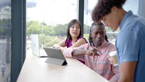 collaborating in office, diverse colleagues discussing project with laptop and coffee cups