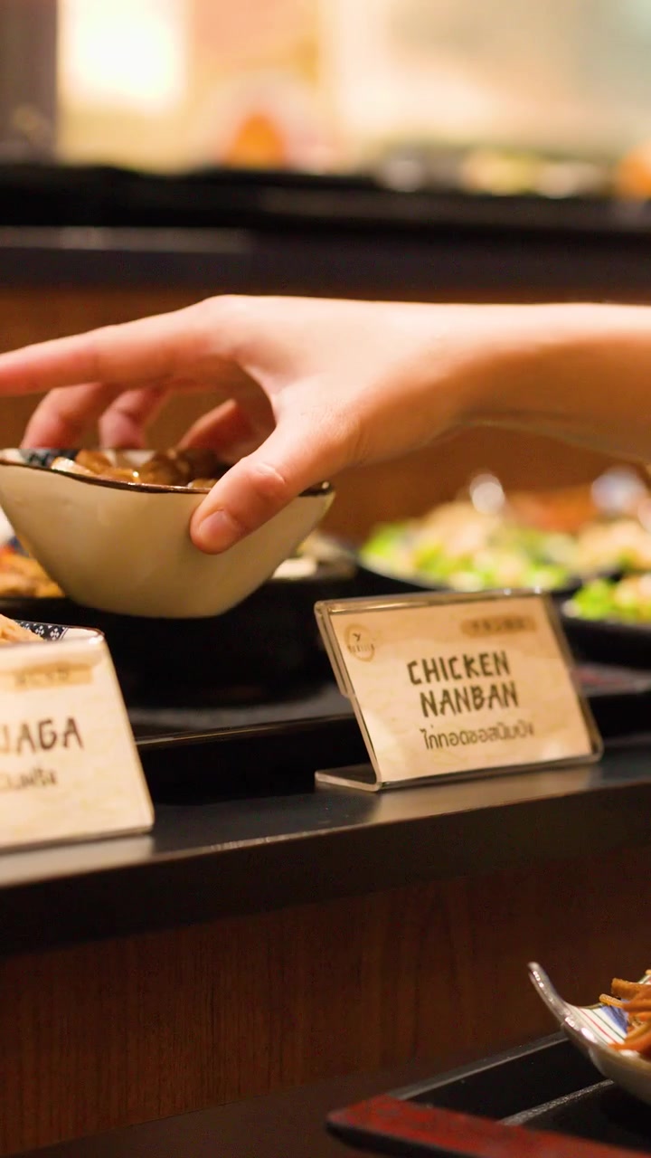 Close-up of a hand selecting a small bowl of fried chicken from a restaurant buffet.