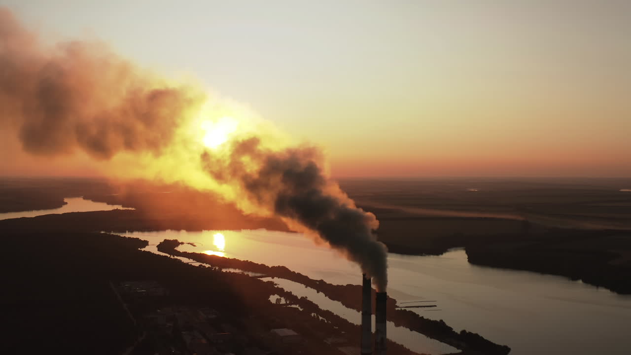 Dirty smoke from industrial chimneys at sunset. Dark chemical fumes released into the atmosphere in the evening. Harmful emissions in the environment. Aerial view.