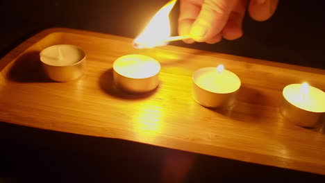 hand with wooden match lights tea candles in decorative wood tray