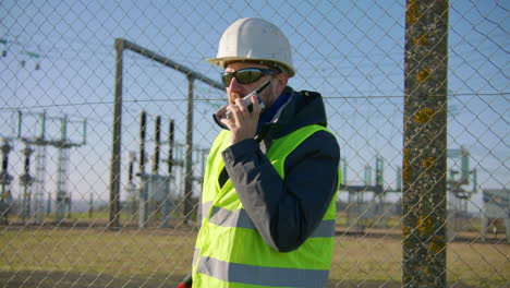 male engineer listening over the walkie talkie while nodding his head at the electric substation, handheld closeup