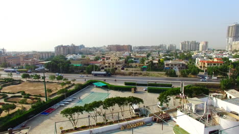 Aerial-of-a-highway-of-the-city-with-traffic-going-on,-under-constructed-building-with-crane-of-its-top,-a-sports-area-and-empty-plot-with-its-roads