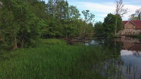 Altes-Haus-An-Einem-Kleinen-Ruhigen-Fluss-In-Skåne,-österlen-Südschweden-Nybroån-Im-Sommer,-Luft-Niedrig-Vorwärts-Langsam