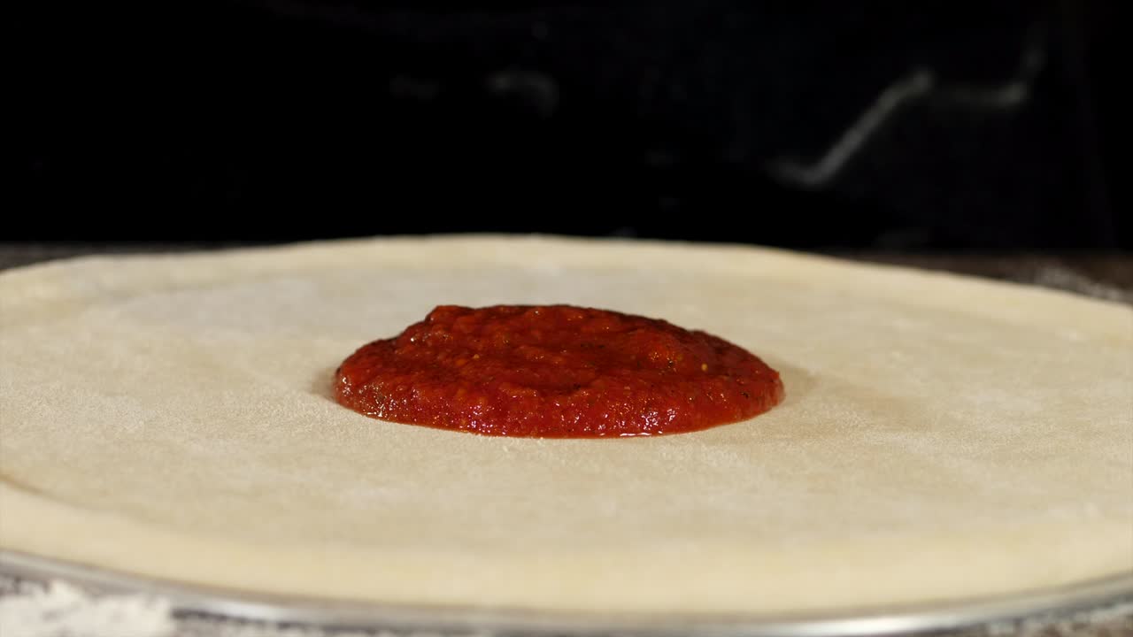 Primo piano della stesura della salsa di pomodoro sull'impasto della pizza