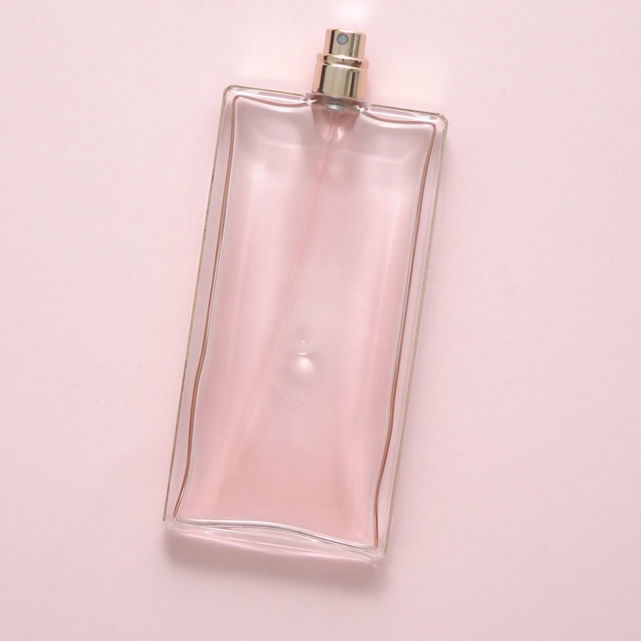 Vista dall'alto di una bottiglia di profumo di lusso su superficie rosa pastello. Composizione minimale. Flat lay