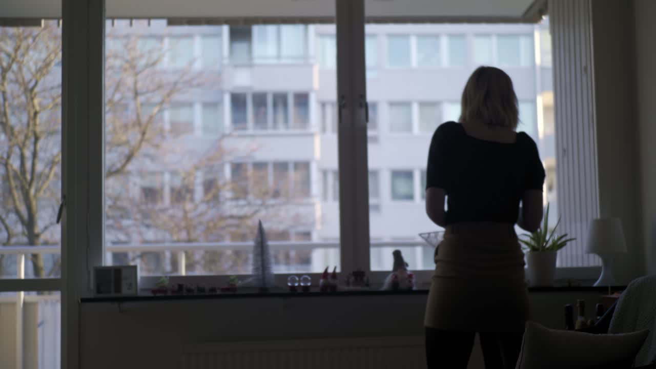 스웨덴의 화창한 겨울날 크리스마스 장식을 들고 아파트 창가를 걷는 젊은 여성, 핸드헬드 와이드 샷 실루엣