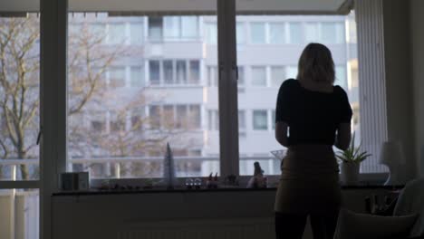 Young-Woman-Walks-By-Apartment-Window-WIth-Christmas-Decorations-On-a-Sunny-Winter-Day-in-Sweden,-Handheld-Wide-Shot-Silhouette