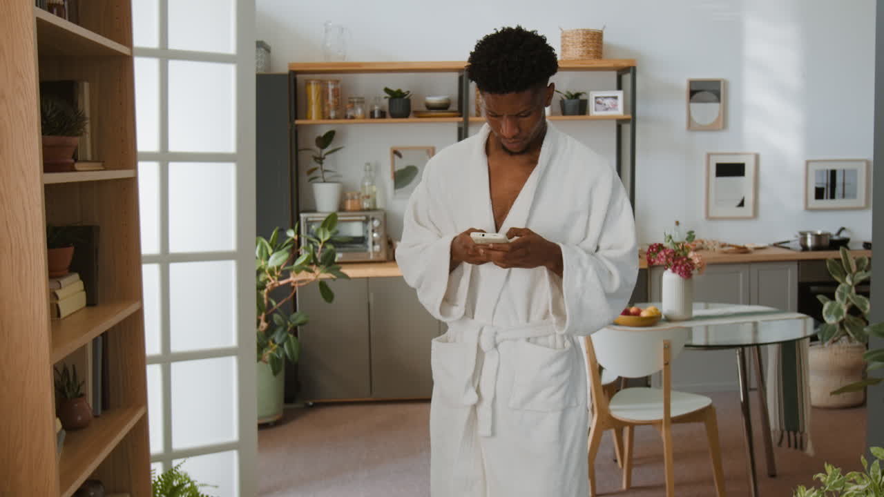 Man in robe using smartphone in kitchen