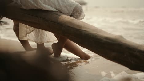 closeup shot of a waves hitting legs of a couple sitting beside seashore on beach.