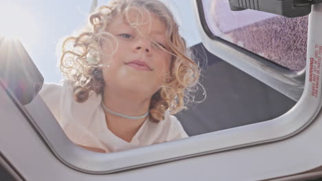 small girl looking through window hatch a yacht in greece