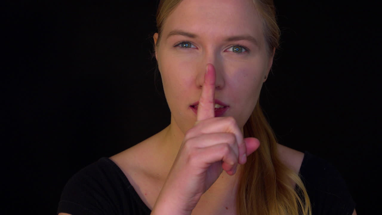 The woman has a secret. A young woman with a mysterious smile puts her finger to her lips as a sign of keeping a secret. The secret is safe. Slowmotion movie