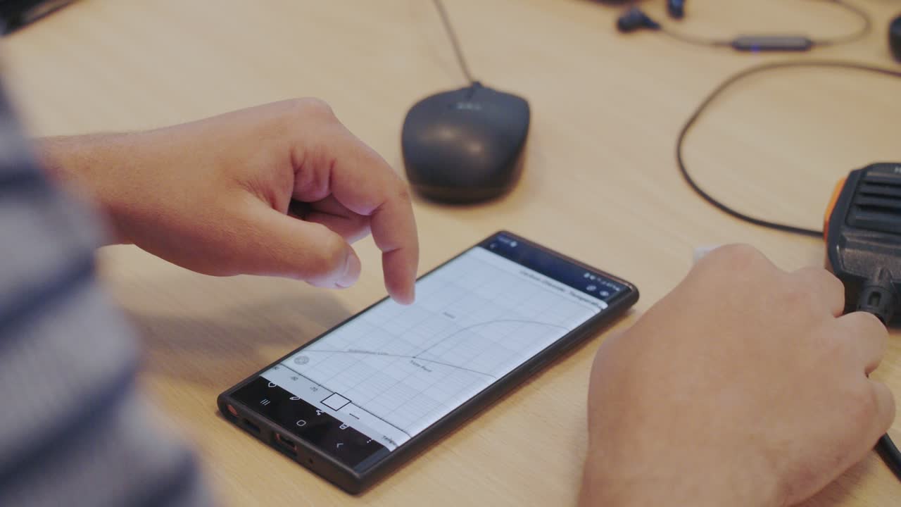 Over-the-shoulder close-up of a person analyzing a data graph on a smartphone. Their finger scrolls and points to the chart, representing business analytics or engineering data