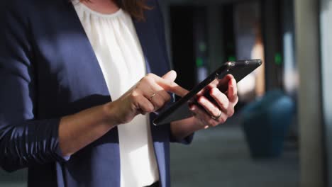sección media de una mujer de negocios caucásica usando una tableta en una oficina moderna