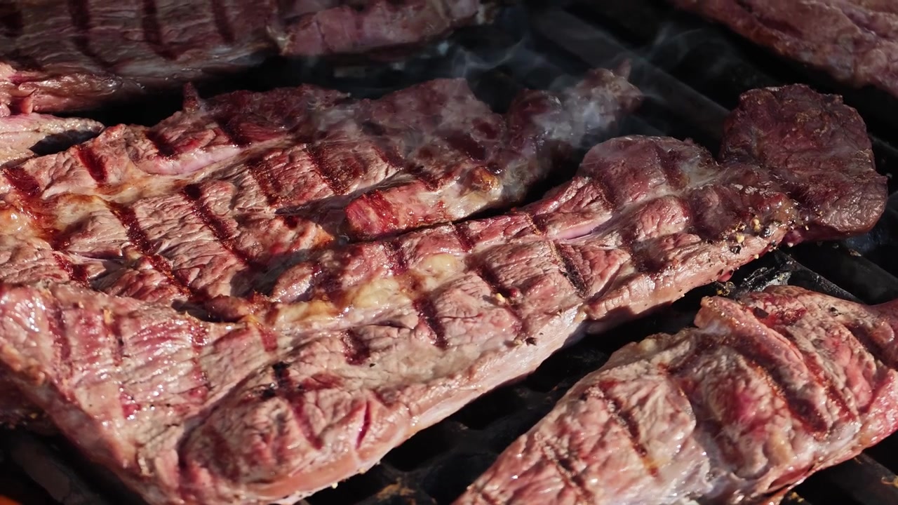Al rallentatore: Bistecca Delmonico Ribeye alla griglia in primo piano con fiamme, condita con sale e pepe. Manzo succoso che cuoce su una griglia BBQ calda, tra fuoco e fumo.