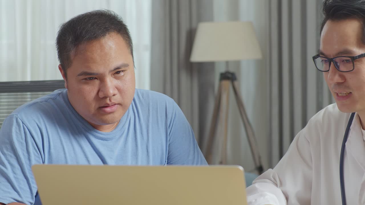 아시안 남성 의사가 클리닉에서 한 남성 환자와 함께 책상에 앉아 노트북에서 의료 검사 결과에 대해 논의하고 나쁜 소식을 전하고 환자를 격려합니다.