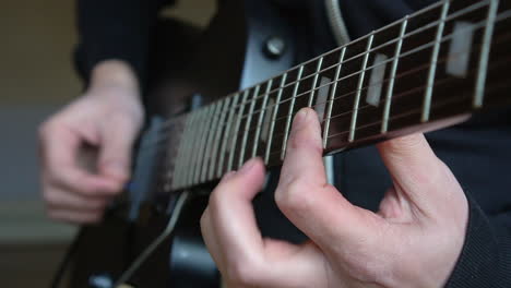 man practising a vintage black electric guitar, rehearsing chords, solos and octaves in a natural light environment.