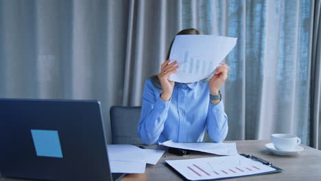 busy lady sitting at desk having lots of work to do. tired female employee throwing papers on the floor with irritation, looking at window thoughtfully.
