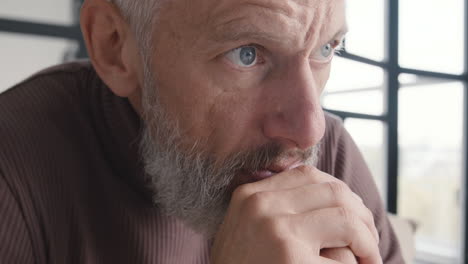 close up of an upset middle aged man worrying and thinking about something while sitting on sofa at home 1