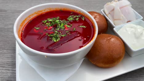 Traditional-Ukrainian-borscht-soup-with-bread-pampushki-buns,-lard-salo-cured-pork-fat-and-sour-cream,-soup-with-beetroot-and-beef,-4K-shot