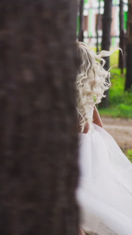 attractive blonde curly haired lady bride wearing gorgeous wedding dress with flowers bouquet runs along summer pine forest slow motion